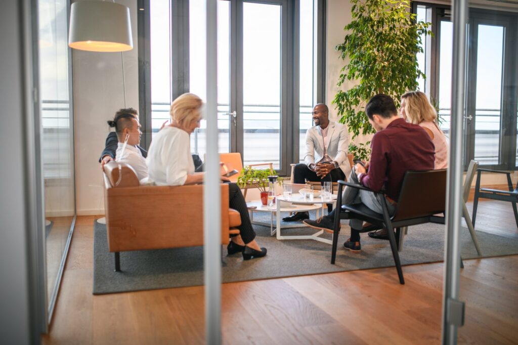 Colleagues meeting informally in a bright office lounge with armchairs and plants