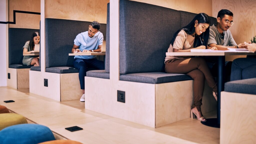 People working in individual focus booths and a shared table in a modern office