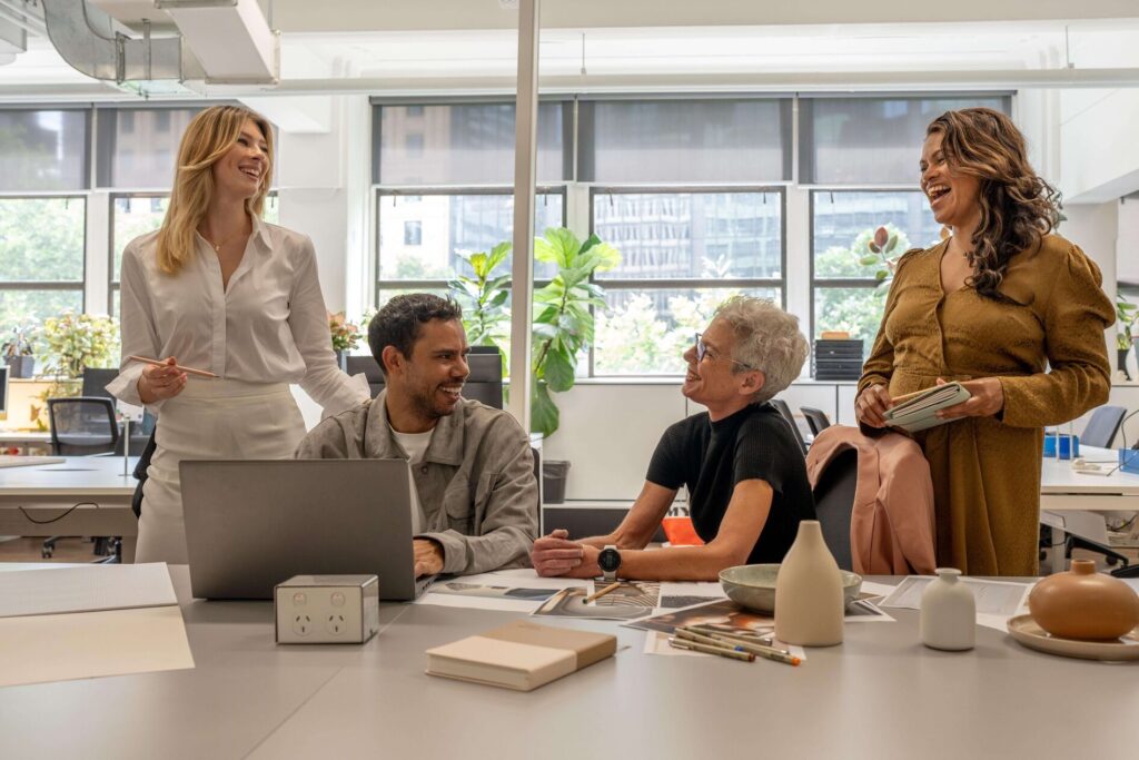 Smiling colleagues talking around a shared desk in a bright, open-plan office