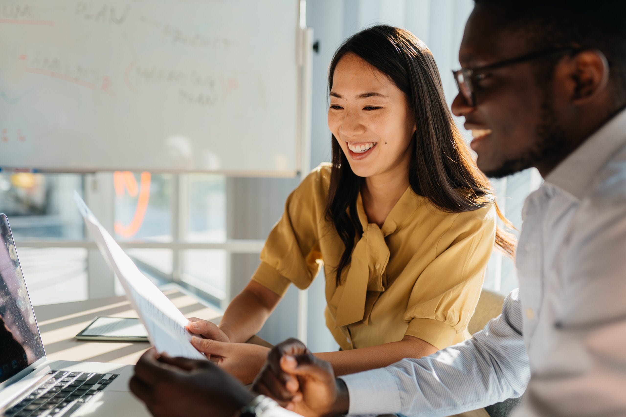 Smiling colleagues reviewing a document together at a sunlit office desk