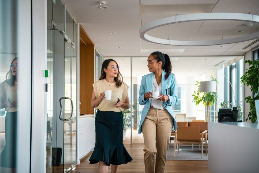 Two colleagues chatting over coffee as they walk through a bright modern office