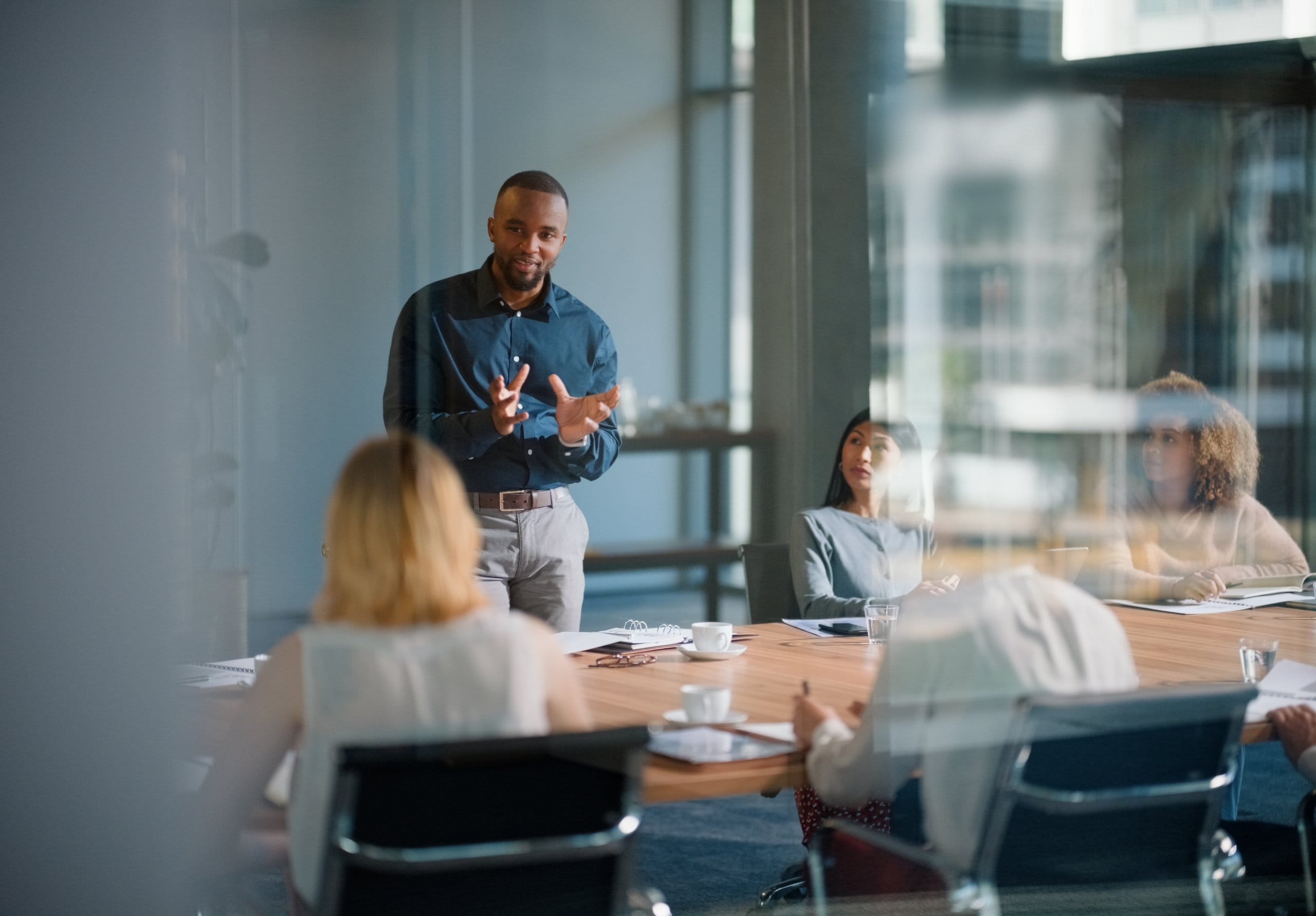 Leader speaking with colleagues around a conference table in a glass-walled meeting room